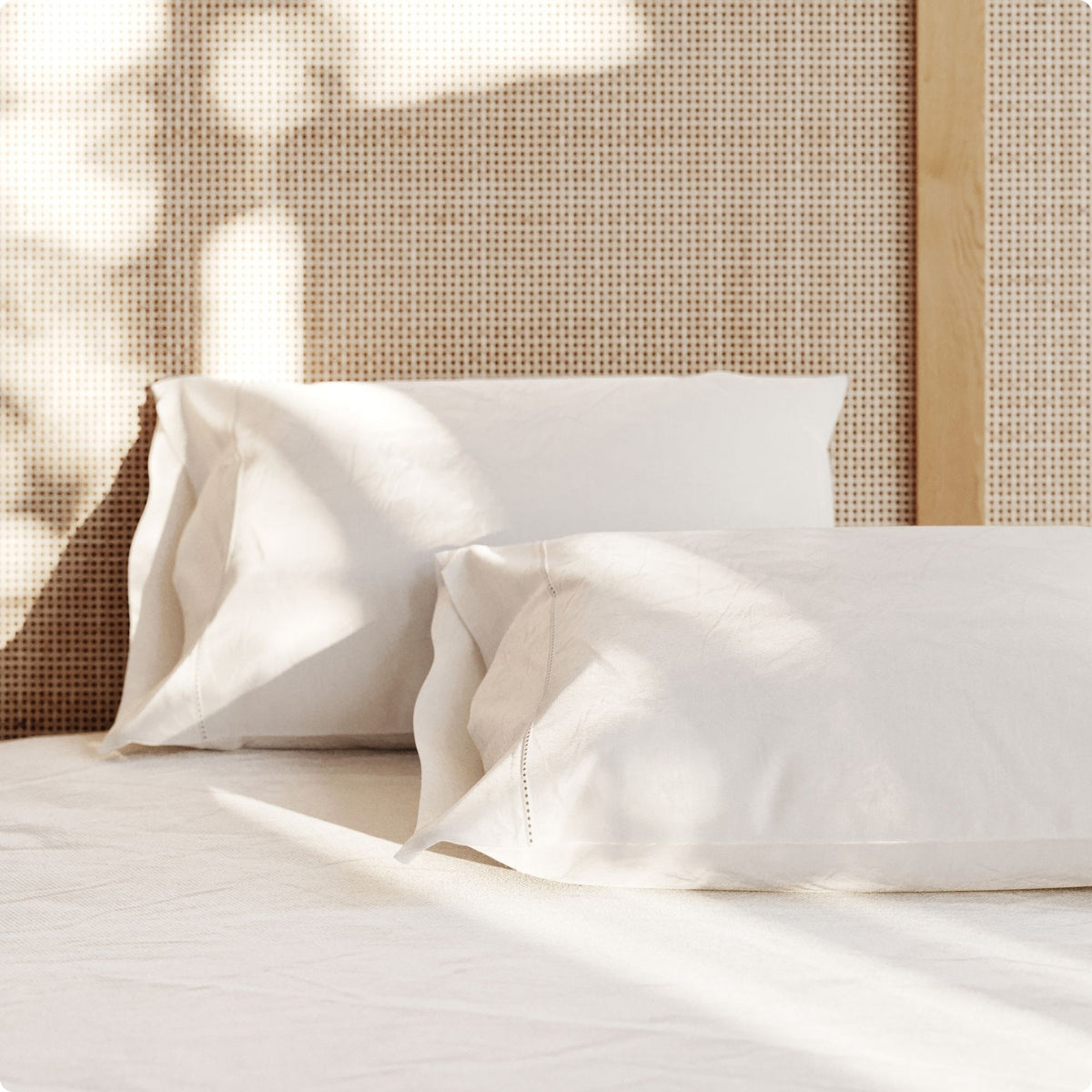 Two white pillows on a bed with a woven headboard.