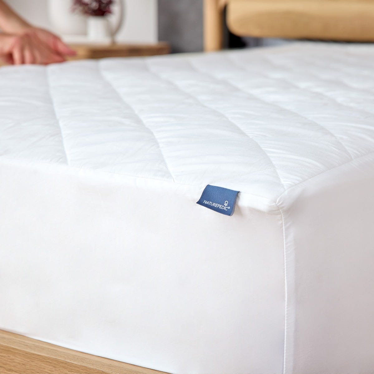 White mattress pad with a brand label on a bed