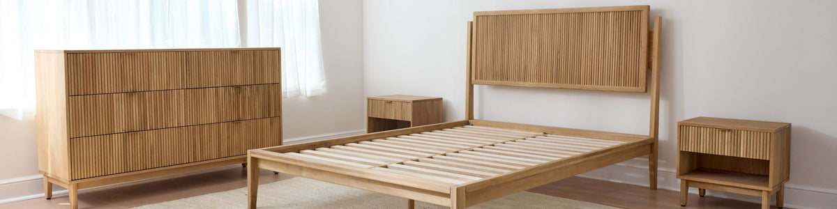 Wooden bedroom furniture set including a bed, dresser, and nightstands in a room with white walls and a window.