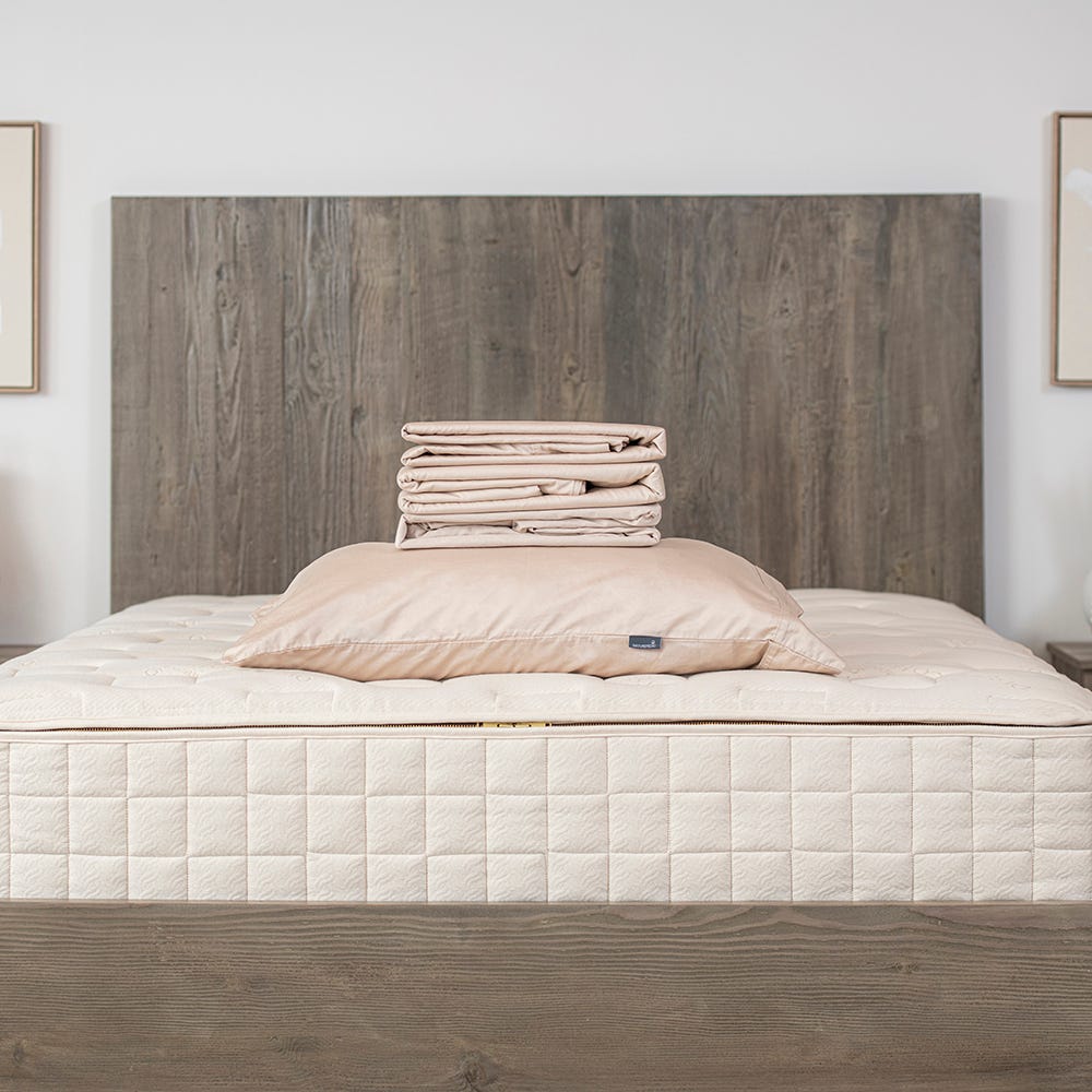Bare mattress on a bed with wooden headboard and white walls