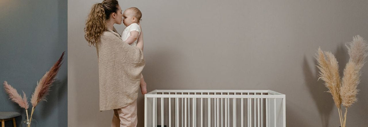 Mother standing near crib and cuddling her baby