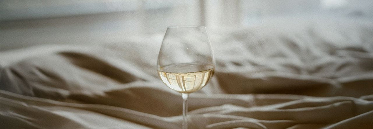 glass of white wine on a bed