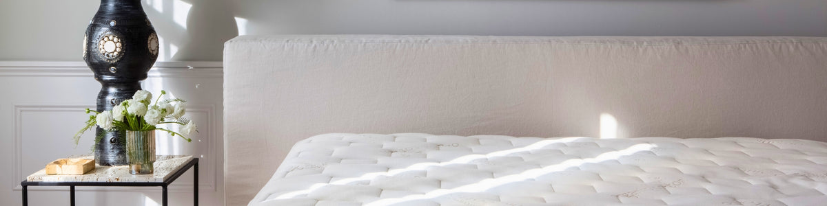 White mattress on a bed with a nightstand and decorative items in a bedroom setting.