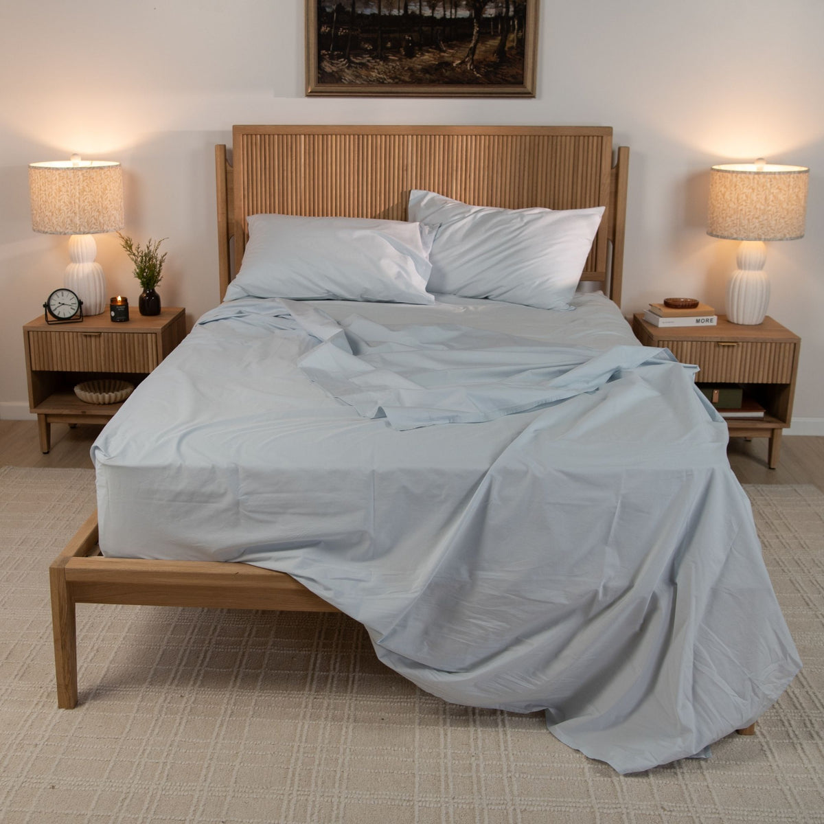 Bedroom with wooden bed frame, light blue bedding, and two nightstands with lamps.