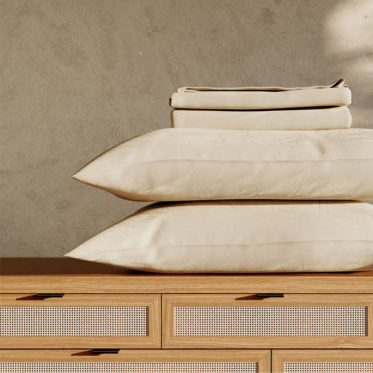 Beige pillows and sheets, stacked on a wooden bed with a neutral background #color_undyed