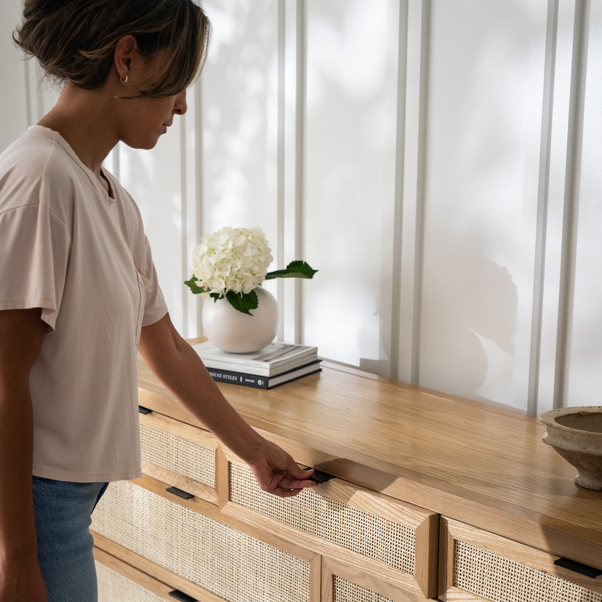 Woman opening the top drawer of the Arienzo dresser with rattan-front drawers.