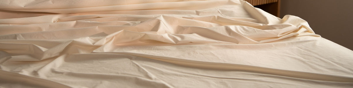 Sateen bed sheets in natural on a bed with a wooden headboard.