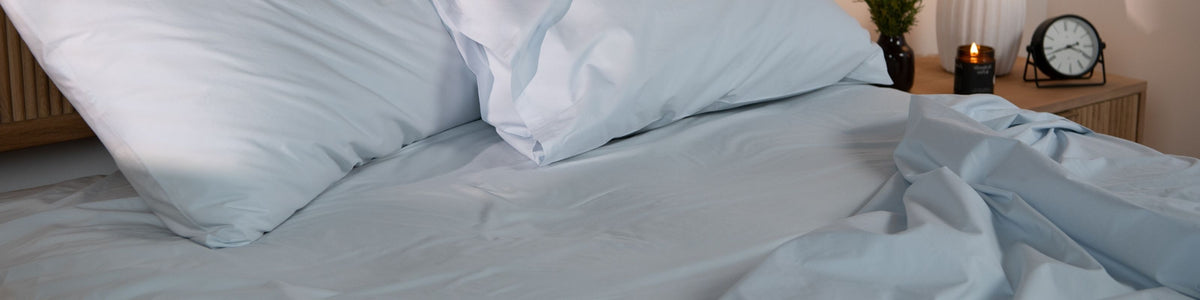 Neatly made bed with pillows and light blue sheets in a bedroom setting.