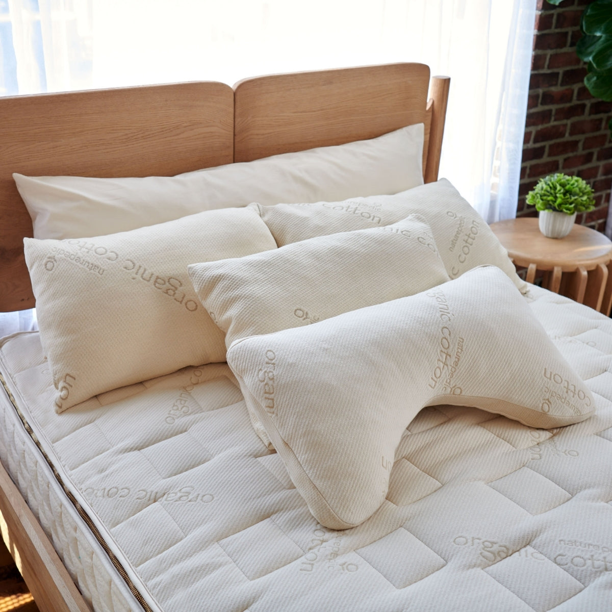 White pillows on a mattress with a wooden headboard and plant in the background
