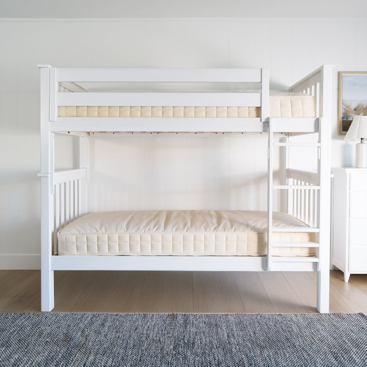 White wooden bunk bed with bare mattresses in a bright, minimalist bedroom setting. #color_washed white  #size_Twin/Twin Bunk 
