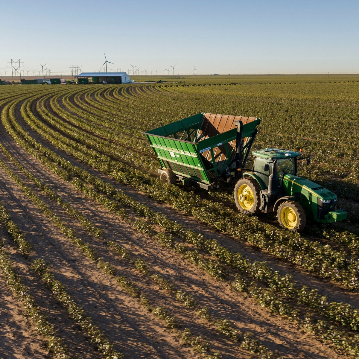 Green tractor with a trailer in a field with wind turbines in the background